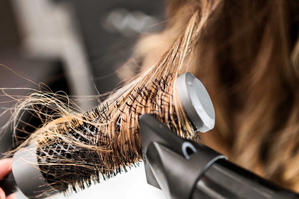 O cabeleireiro usa um secador de cabelo e modela o cabelo de uma